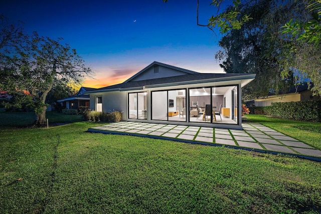 back house at dusk featuring a lawn and a patio area