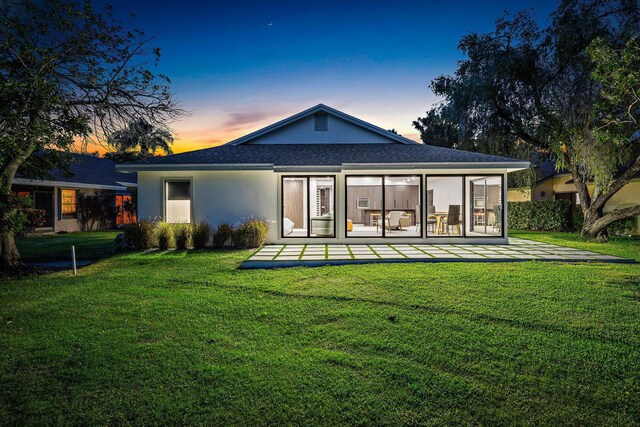 back house at dusk featuring a patio and a lawn