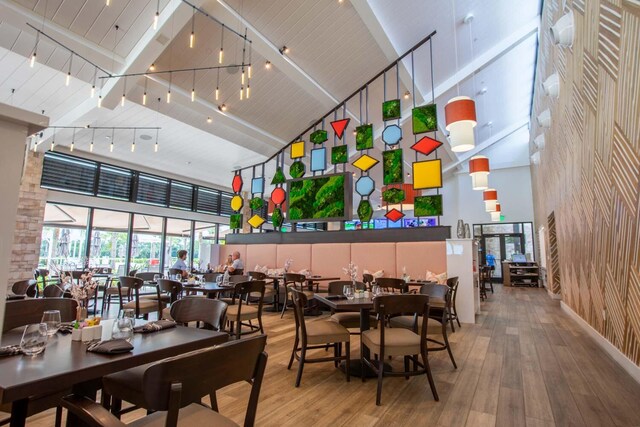 dining space featuring beam ceiling, rail lighting, high vaulted ceiling, brick wall, and light wood-type flooring