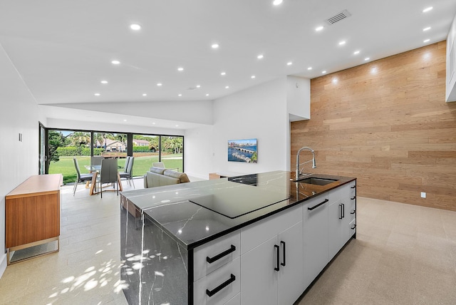 kitchen featuring wooden walls, white cabinetry, lofted ceiling, sink, and a large island