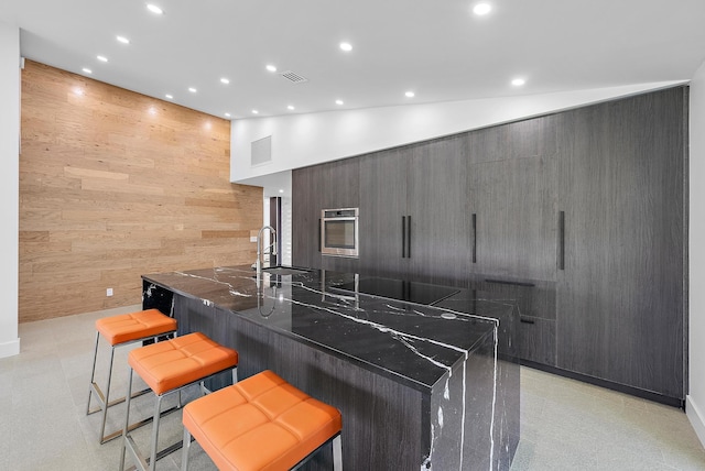 kitchen with a kitchen breakfast bar, wooden walls, oven, sink, and black electric stovetop