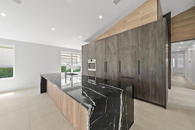 kitchen featuring dark stone counters, stainless steel oven, lofted ceiling, and a spacious island