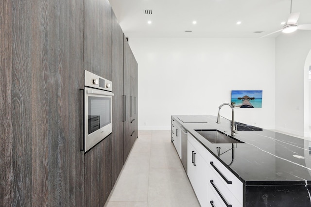 kitchen with dark stone countertops, appliances with stainless steel finishes, an island with sink, sink, and white cabinetry