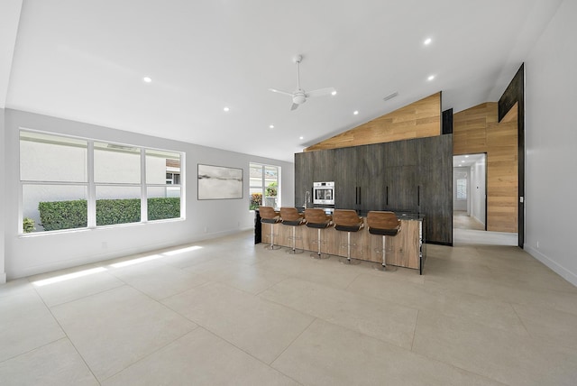 unfurnished living room with light tile patterned flooring, high vaulted ceiling, ceiling fan, and wooden walls