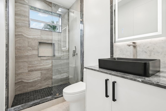 bathroom featuring tile patterned flooring, a tile shower, vanity, and toilet