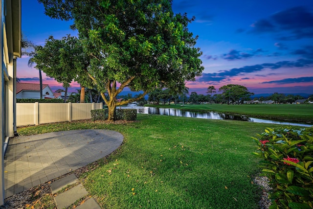 yard at dusk with a patio area and a water view