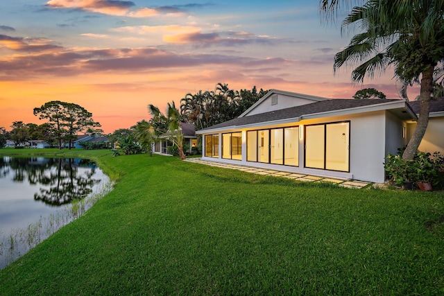 back house at dusk featuring a lawn and a water view