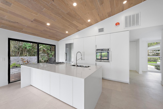 kitchen featuring sink, appliances with stainless steel finishes, white cabinets, wooden ceiling, and a large island with sink