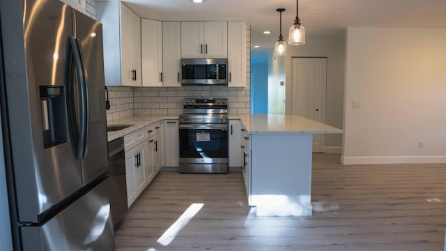 kitchen with light hardwood / wood-style flooring, stainless steel appliances, backsplash, decorative light fixtures, and white cabinetry