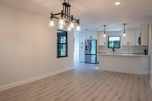 kitchen featuring tasteful backsplash, light wood-type flooring, white cabinets, stainless steel appliances, and hanging light fixtures