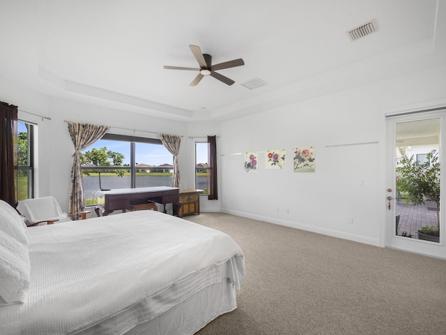 carpeted bedroom with a tray ceiling, ceiling fan, and a water view