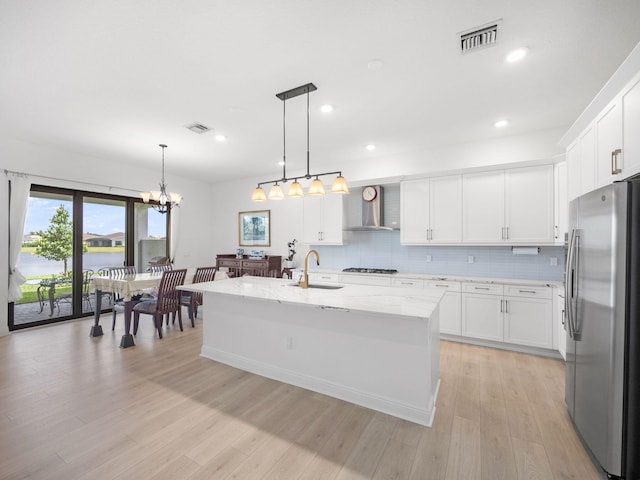 kitchen featuring wall chimney exhaust hood, light hardwood / wood-style floors, a center island with sink, white cabinets, and appliances with stainless steel finishes