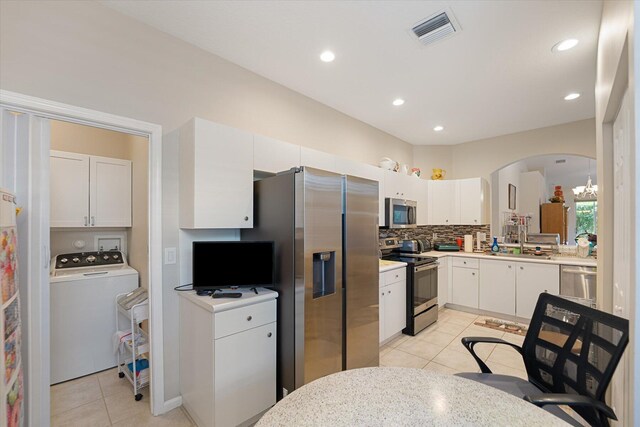 kitchen with stainless steel appliances, washer / dryer, decorative backsplash, light tile patterned flooring, and white cabinetry