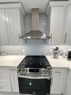 kitchen with wall chimney exhaust hood, white cabinetry, decorative backsplash, and stainless steel electric range oven