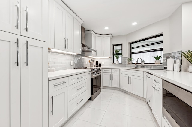 kitchen with white cabinets, wall chimney range hood, sink, appliances with stainless steel finishes, and light tile patterned flooring