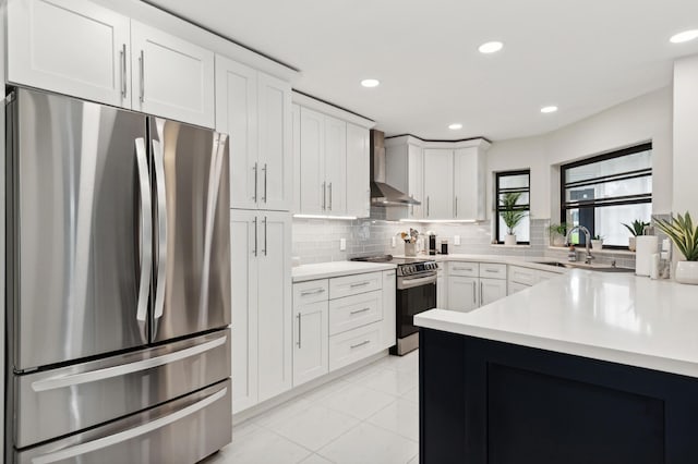 kitchen with appliances with stainless steel finishes, light countertops, a sink, and wall chimney range hood