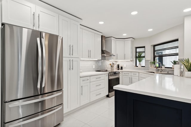 kitchen with decorative backsplash, appliances with stainless steel finishes, sink, wall chimney range hood, and white cabinets