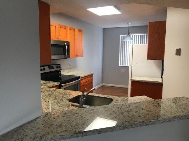 kitchen with light stone countertops, appliances with stainless steel finishes, wood-type flooring, decorative light fixtures, and sink