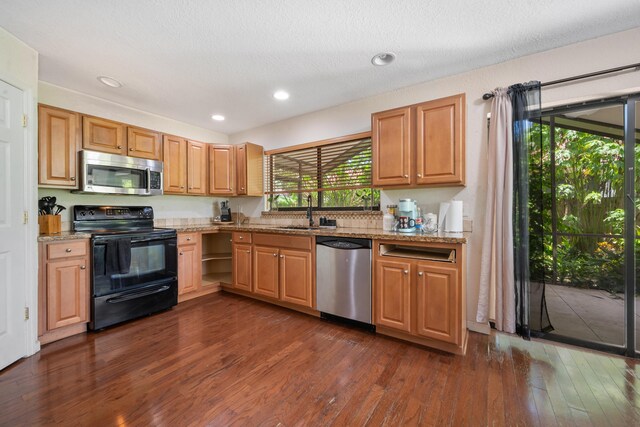 kitchen with sink, appliances with stainless steel finishes, light stone counters, and dark hardwood / wood-style floors