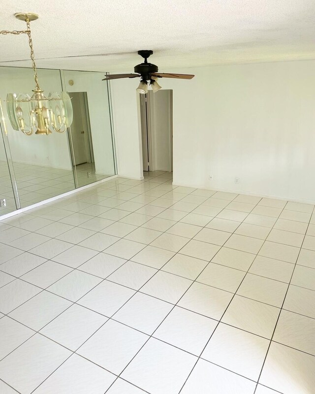 tiled empty room featuring ceiling fan with notable chandelier and a textured ceiling