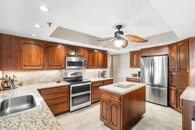 kitchen with sink, stainless steel appliances, a raised ceiling, and a kitchen island