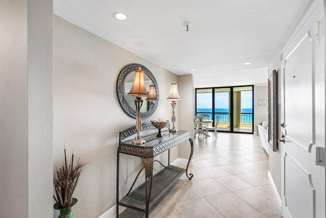 hallway featuring expansive windows, a water view, light tile patterned floors, and a textured ceiling