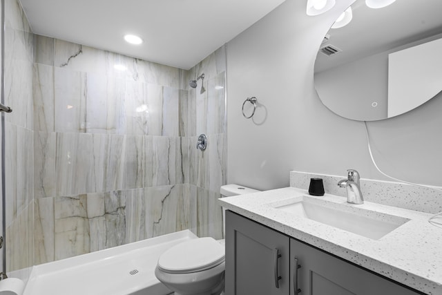 bathroom featuring vanity, a tile shower, and toilet