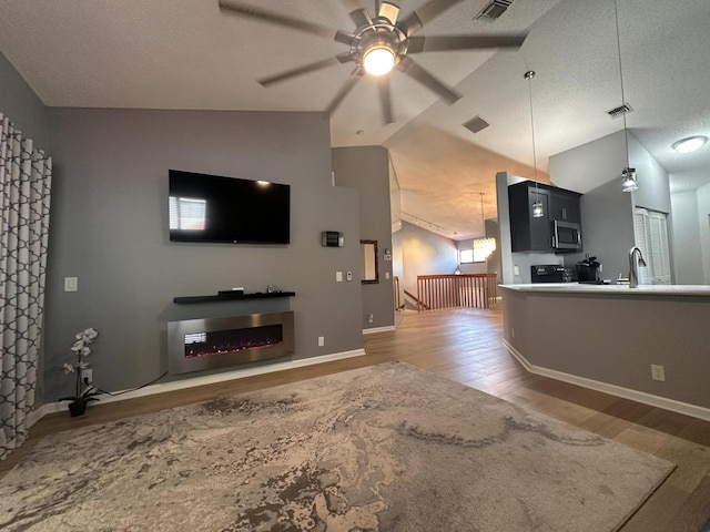 living room with lofted ceiling, hardwood / wood-style floors, a textured ceiling, and ceiling fan