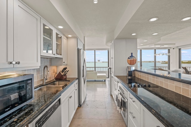 kitchen with light tile patterned flooring, backsplash, a water view, appliances with stainless steel finishes, and sink