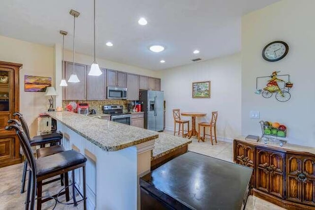 kitchen with a breakfast bar area, a peninsula, hanging light fixtures, stainless steel appliances, and backsplash