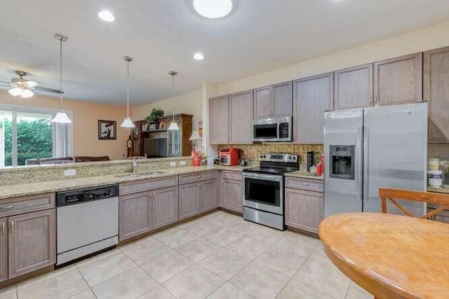 kitchen featuring a peninsula, a sink, hanging light fixtures, appliances with stainless steel finishes, and decorative backsplash