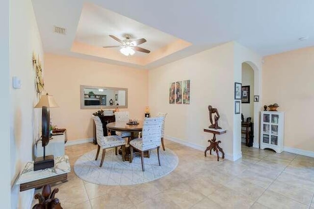 dining area featuring a tray ceiling, arched walkways, visible vents, a ceiling fan, and baseboards