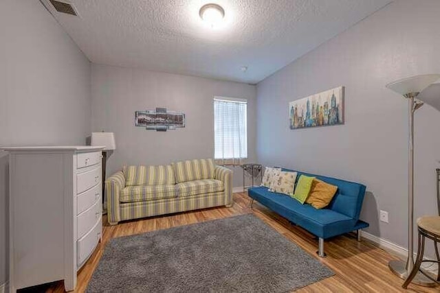 living area featuring a textured ceiling, wood finished floors, visible vents, and baseboards