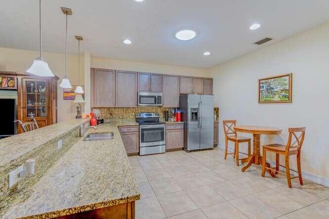 kitchen with appliances with stainless steel finishes, tasteful backsplash, light stone counters, sink, and decorative light fixtures