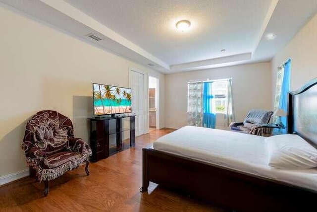 bedroom featuring a tray ceiling, wood finished floors, visible vents, and baseboards