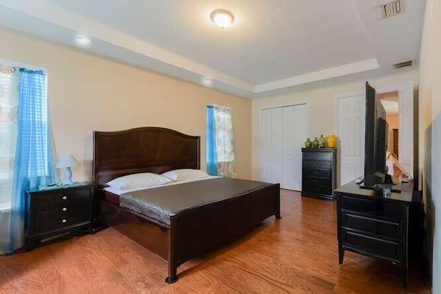 bedroom featuring a raised ceiling, visible vents, two closets, and wood finished floors