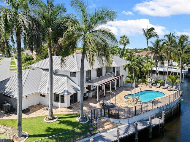 rear view of property with central AC unit, a patio, a fenced in pool, a water view, and a lawn