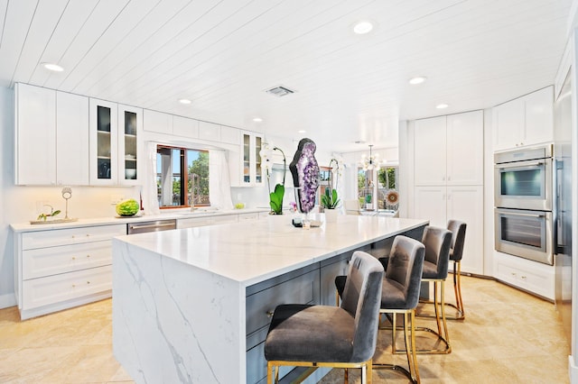 kitchen with appliances with stainless steel finishes, a large island, light stone countertops, and white cabinetry