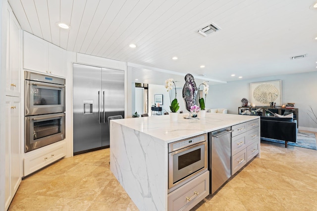 kitchen with stainless steel appliances, a center island, white cabinets, light tile patterned flooring, and light stone counters