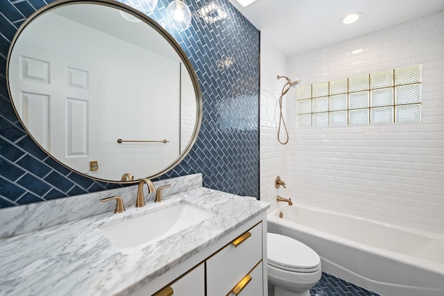 full bathroom featuring tile walls, vanity, tiled shower / bath, and toilet