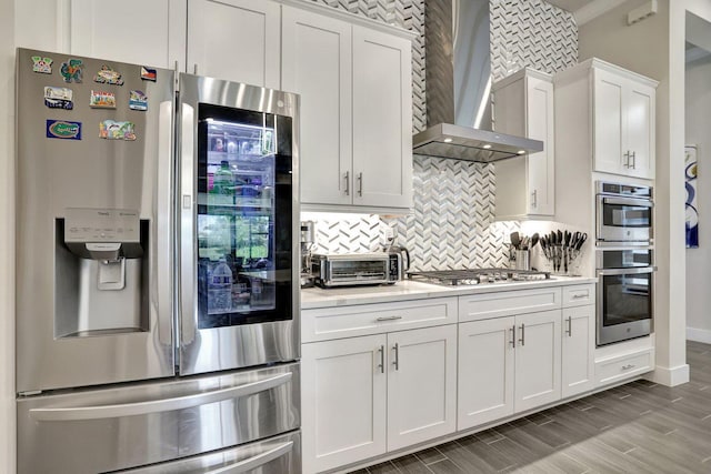 kitchen with wall chimney exhaust hood, appliances with stainless steel finishes, backsplash, and white cabinets