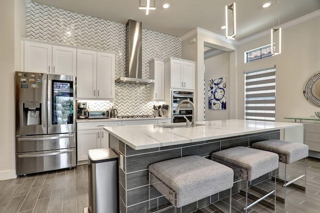 kitchen with a kitchen island with sink, white cabinets, wall chimney exhaust hood, and appliances with stainless steel finishes