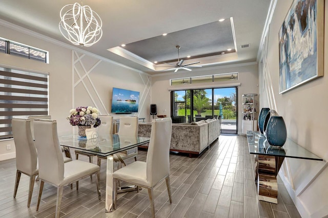 dining space featuring a raised ceiling, ornamental molding, and ceiling fan with notable chandelier