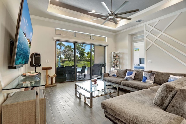 living room featuring crown molding, ceiling fan, hardwood / wood-style floors, a high ceiling, and a tray ceiling