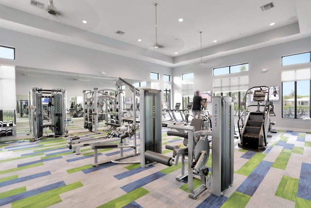 exercise room featuring light colored carpet, ceiling fan, and a high ceiling