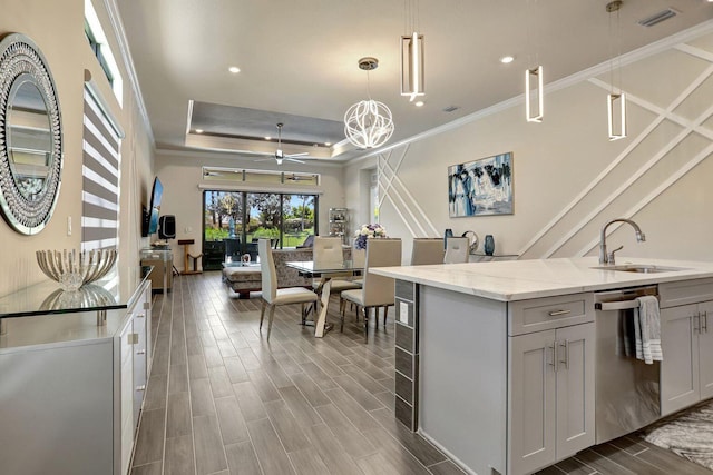 kitchen with decorative light fixtures, dishwasher, sink, a kitchen island with sink, and a raised ceiling