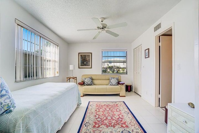 tiled bedroom with ceiling fan, a textured ceiling, a closet, and multiple windows