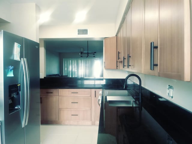 kitchen with light tile patterned floors, light brown cabinetry, stainless steel fridge with ice dispenser, and sink