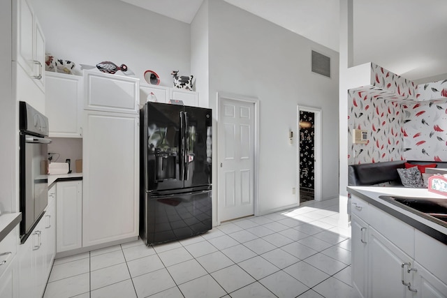 kitchen featuring white cabinets, a high ceiling, black fridge with ice dispenser, stainless steel oven, and light tile patterned flooring