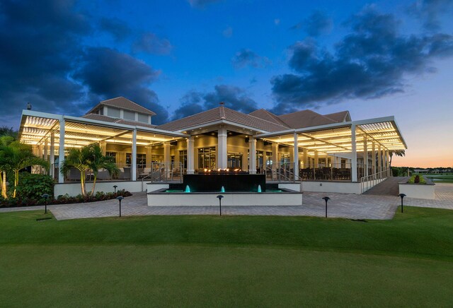 back house at dusk featuring a patio area and a lawn